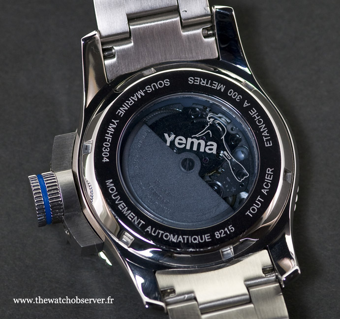 Le fond transparent, esthétiquement très cohérent avec le côté ludique de la montre, est coloré en bleu/gris et reprend la marque Yema agrémentée d'un plongeur stylisé.